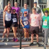 9 staff members in running shorts and sneakers with race numbers on their shirts