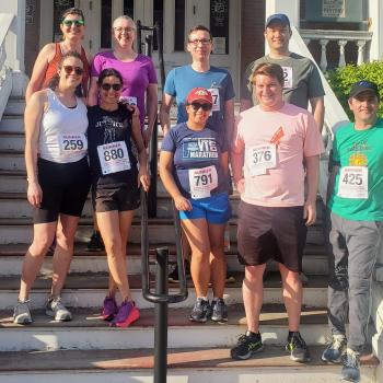 9 staff members in running shorts and sneakers with race numbers on their shirts